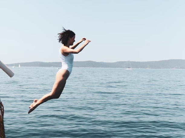 Frau springt im weißen Badeanzug ins Meer
