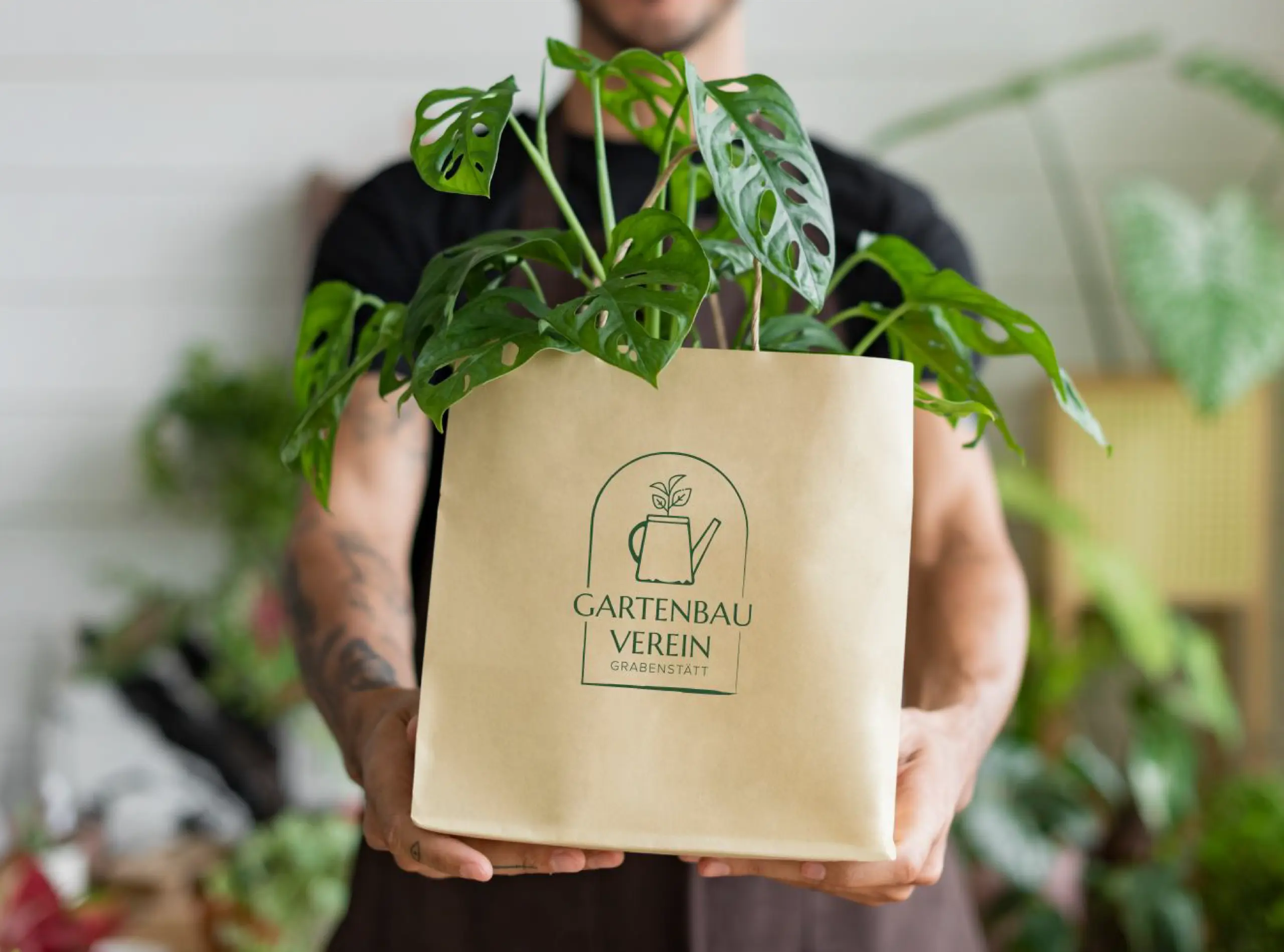 Gartenbauverein Grabenstätt Brand Design auf Papiertüte mit Monstera Pflanze von einem Mann gehalten
